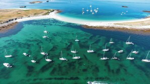 Ein Luftbild einer Küstenregion mit zahlreichen Segelbooten, die in klarem, türkisblauem Wasser vor Anker liegen.
