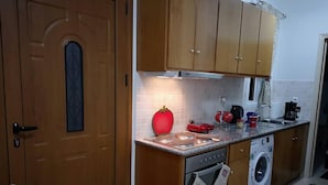 A compact kitchen with wooden cabinets, a built-in oven, a washing machine, and a red decorative item on the countertop. - Apartment - Sleeps 5 - Parking - Private Terrace (Kalymnos)