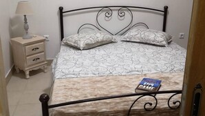 A bed with a patterned bedspread and pillows, a bedside table with a lamp, and a book titled 'David Baldacci: Fair Game' on the bed. - Apartment - Sleeps 5 - Parking - Private Terrace (Kalymnos)