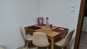 A small dining area with a wooden table, four chairs, a box of breakfast cereal, a bottle, and a remote control. - Apartment - Sleeps 5 - Parking - Private Terrace (Kalymnos)
