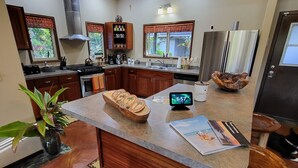 A modern kitchen with a central island, wooden stools, a built-in oven, and a ceiling fan. - Lava House (Pahoa)