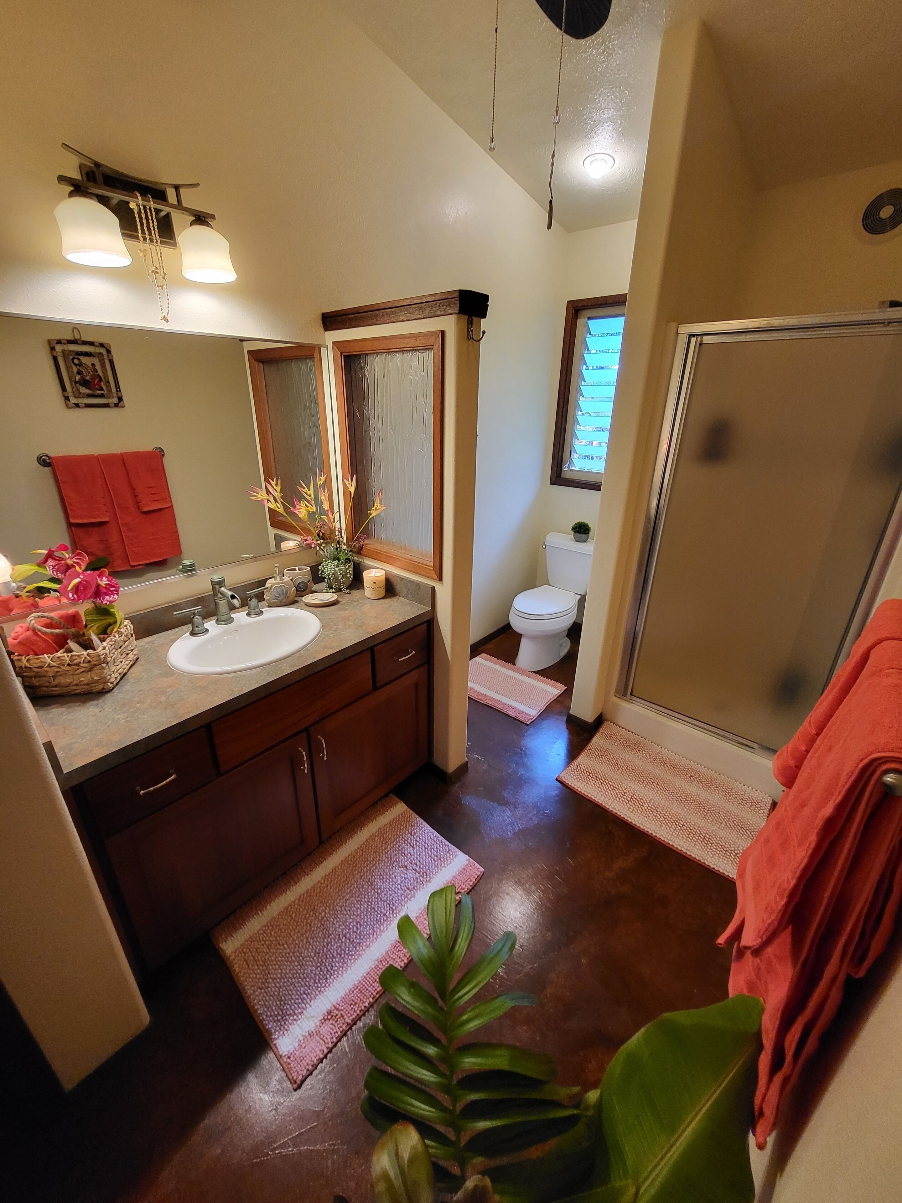 Baño con lavamanos, espejo e inodoro. Cuenta con una zona de ducha con puerta de vidrio.