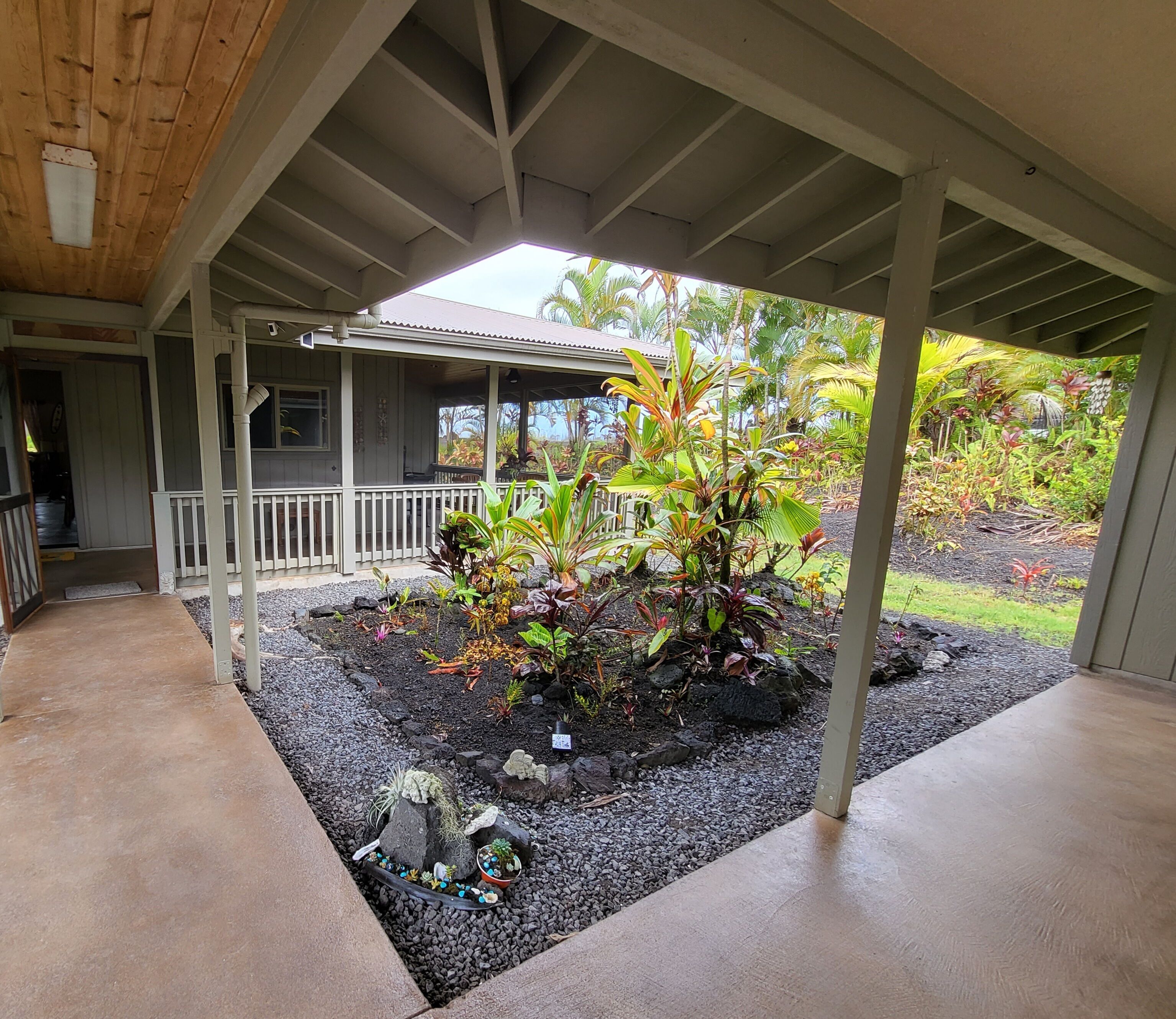 Un espace extérieur abrité comprenant un jardin, une terrasse en bois et un bâtiment en arrière-plan.