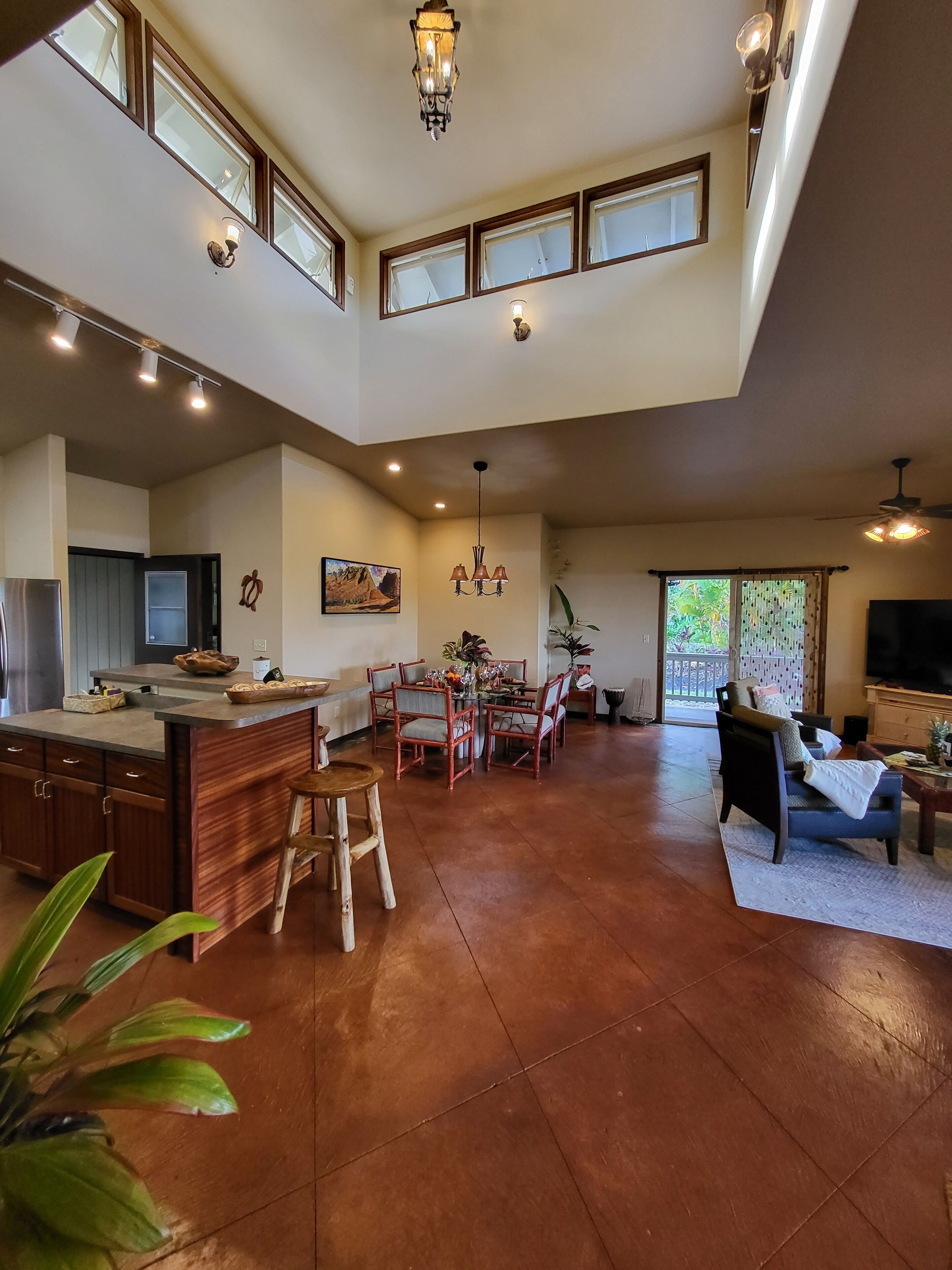 A spacious kitchen with a dining area, a living room with a sofa and TV, and a large window providing natural light.