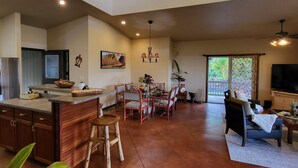 A spacious kitchen with a dining area, a living room with a sofa and TV, and a large window providing natural light. - Lava House (Pahoa)