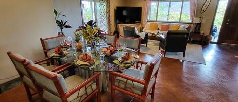 Un coin repas avec une table en verre entourée de chaises en bois, un lustre et un téléviseur en arrière-plan.