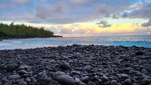 A rocky beach with a view of the ocean and a forested area in the background. - Lava House (Pahoa)