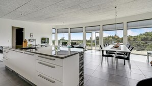 A modern kitchen with a large island, a dining area with a long table and chairs, and large windows offering a view of the outdoors. - 4 bedroom nice home in Ebeltoft (Ebeltoft)