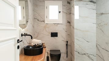 A modern bathroom with a marble floor, a wooden vanity, a black sink, a toilet, and a shower.