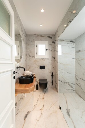 A modern bathroom with a marble floor, a wooden vanity, a black sink, a toilet, and a shower.