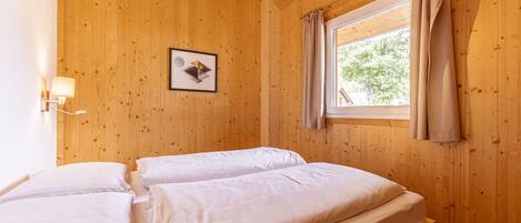 Een houten kamer met twee bedden, een raam met gordijnen, een wandlamp en een ingelijst beeld.