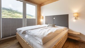 A bedroom with a large bed, wooden headboard, and a view of a green landscape through a window. - Superior Apartment # 2 for up to 6 persons with IR Sauna (St. Georgen am Kreischberg)