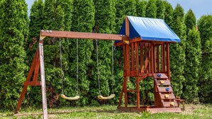Een houten schommelset met een blauw dak en een klimladder.