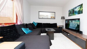 Een moderne woonkamer met een hoekbank, een flatscreen televisie, een salontafel en een grote spiegel aan de muur.