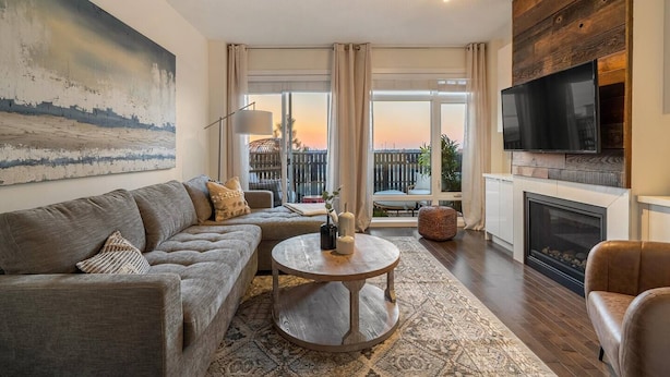 A modern living room with a sectional sofa, a round coffee table, a fireplace, and a large TV mounted on a wooden wall.