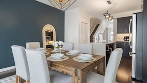 A modern dining area with a wooden table set for six, white chairs, and a decorative mirror above the table.
