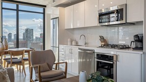 Une cuisine moderne avec des armoires blanches, des appareils en acier inoxydable et une vue sur la ville grâce à de grandes fenêtres.