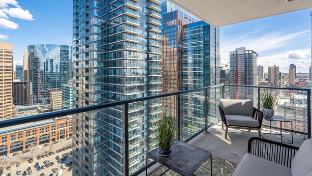 Un immeuble de grande hauteur doté d’un balcon aménagé avec un coin salon, un pot de fleurs et une vue sur le paysage urbain.