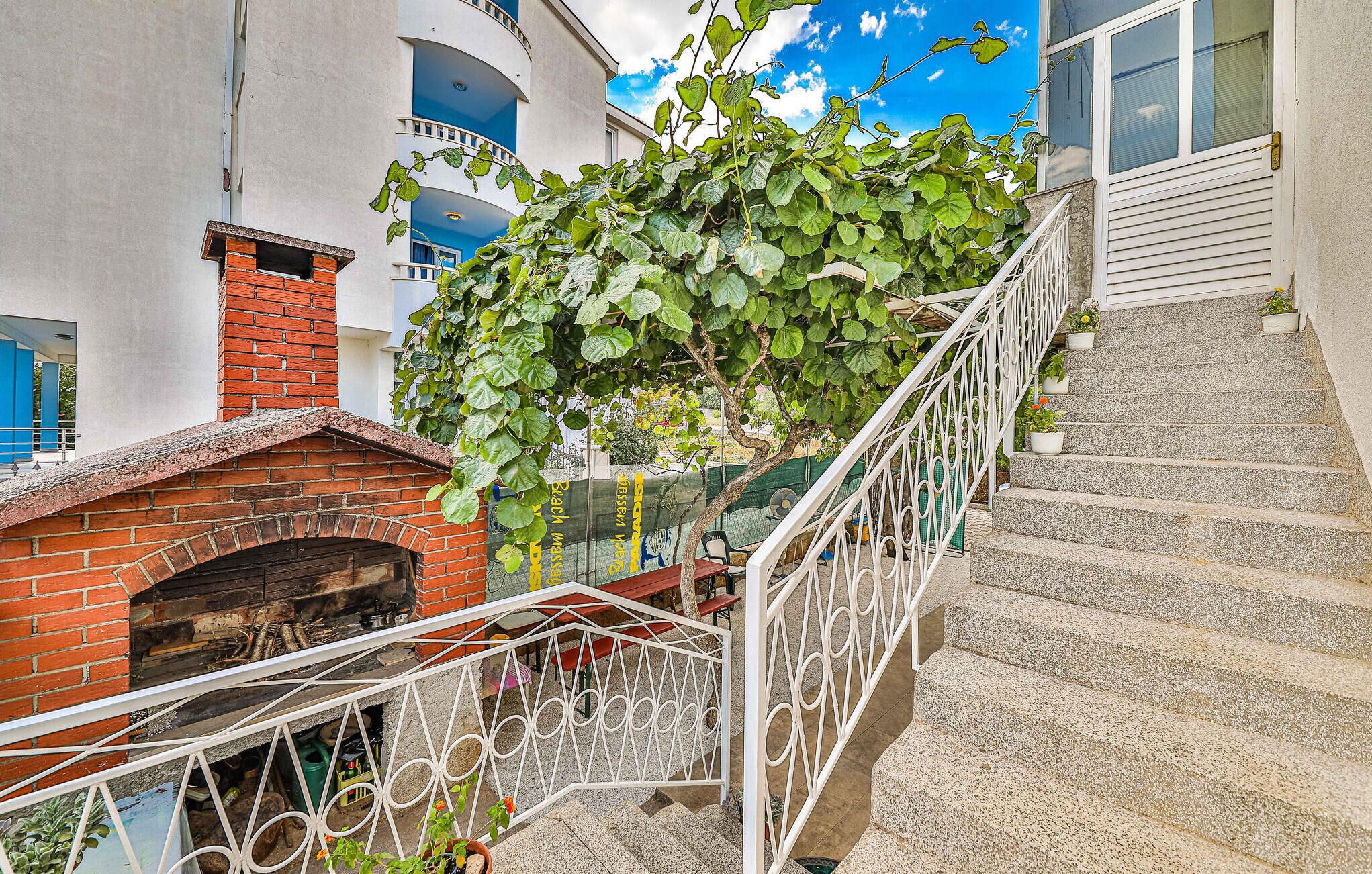 A staircase with a white metal railing, a brick fireplace, and a green vine climbing over the railing.