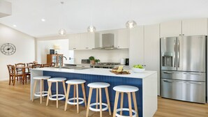 A modern kitchen with a central island, bar stools, stainless steel appliances, and a dining area with wooden chairs. - The Hideaway at Sutton Forest Retreat (Sutton Forest)