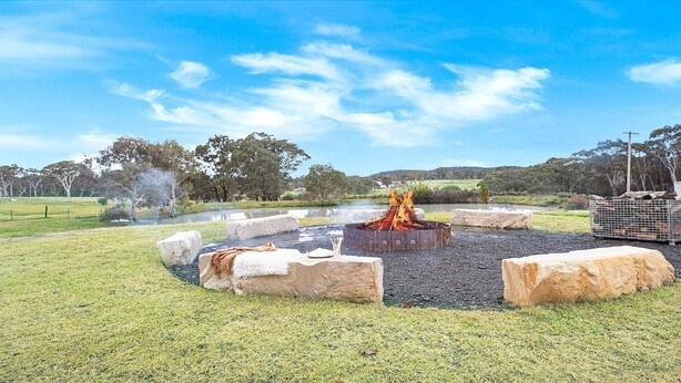 A fire pit surrounded by rocks in a grassy area with trees and a clear sky in the background. - The Hideaway at Sutton Forest Retreat (Sutton Forest)
