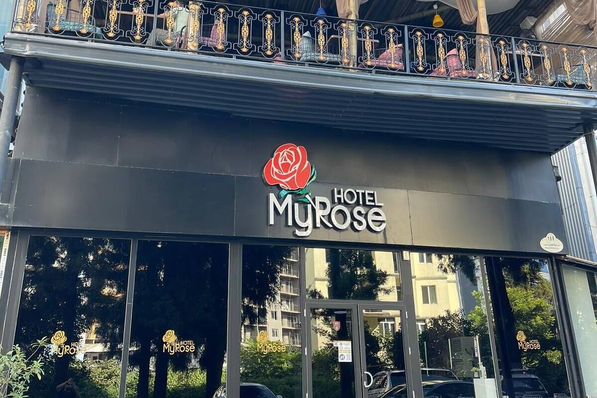 A hotel with a balcony, outdoor seating, and a rose logo.