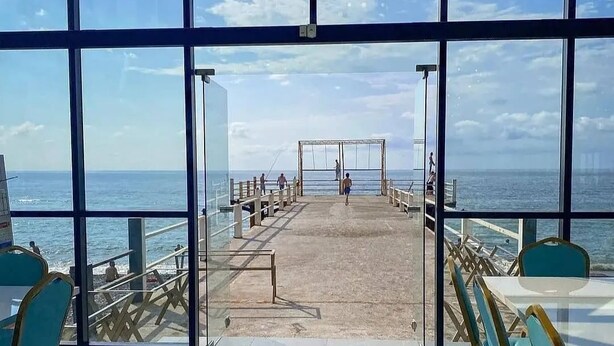 A view from inside a building with large windows overlooking a pier and the ocean. - Hotel MyRose (Batumi)