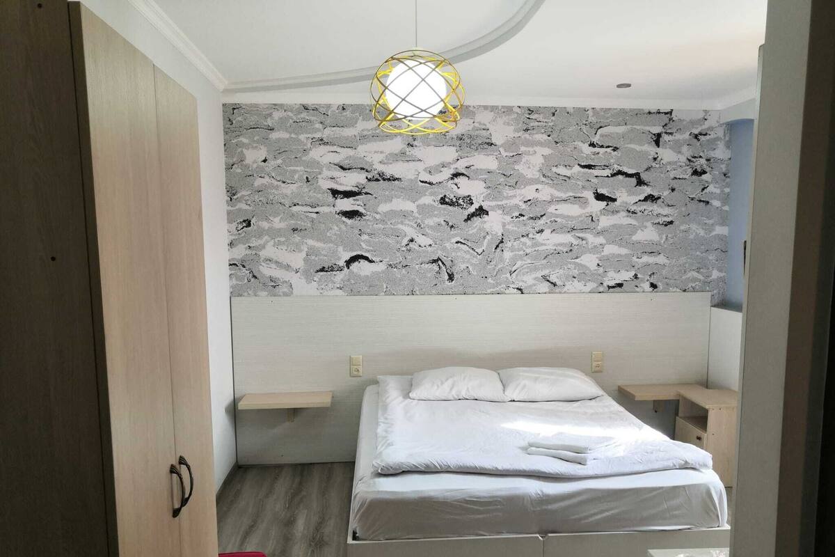 A bedroom with a stone-patterned wall, a bed with white bedding, a bedside table, and a hanging light fixture.