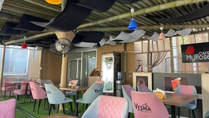 An outdoor cafe with tables and chairs, a fan, and a sign for 'Cafe MyRose'. - Hotel MyRose (Batumi)