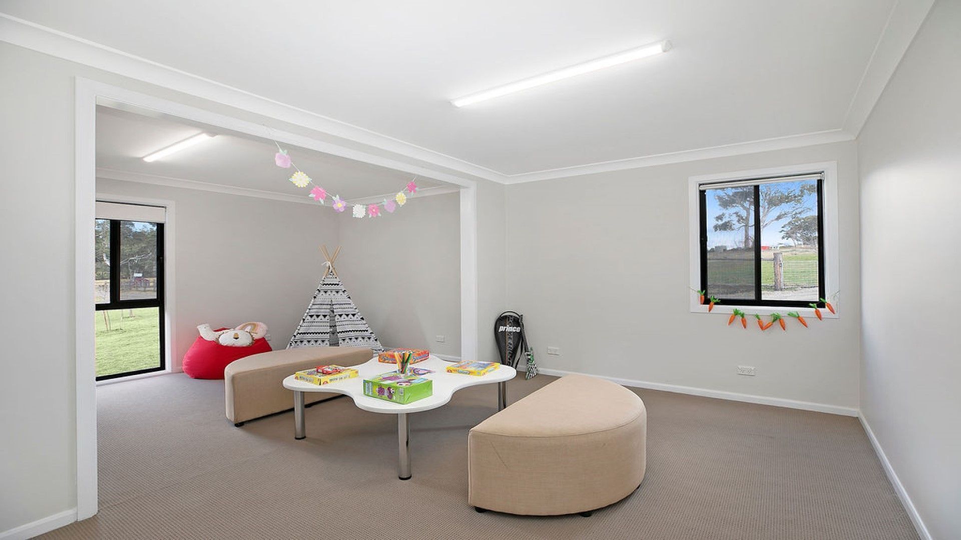 A spacious room with a large window, a white ceiling, and a cozy seating area with a table and ottoman.