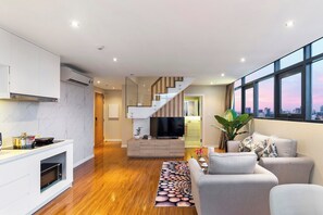 Una sala de estar moderna con chimenea empotrada, televisor de pantalla plana y una escalera que lleva a un nivel superior.