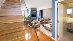 A modern interior with a wooden staircase, a living area with a sofa and coffee table, and a kitchen with a sink and countertop.