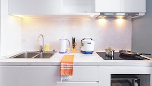 A modern kitchen with a double sink, a built-in oven, a kettle, a rice cooker, and a frying pan on an induction cooktop.