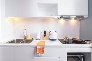 A modern kitchen with a double sink, a built-in oven, a kettle, a rice cooker, and a frying pan on an induction cooktop.