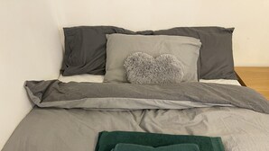 Ein ordentlich bezogenes Bett mit grauer Bettwäsche und einem grünen Handtuch.
