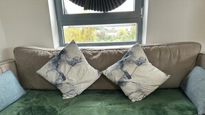 Ein beiges Sofa mit einer grünen Decke und zwei dekorativen Kissen mit Marmormuster.