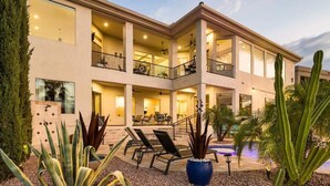 A multi-story house with a balcony, outdoor seating, and a pool.