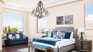 A bedroom with a bed, a bench, a sofa, a chandelier, and artwork on the wall.