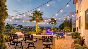 An outdoor bar area with chairs, a pool, and string lights.
