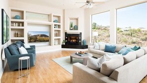 A spacious living room with a fireplace, two sofas, a coffee table, and a large window offering a view of the desert.
