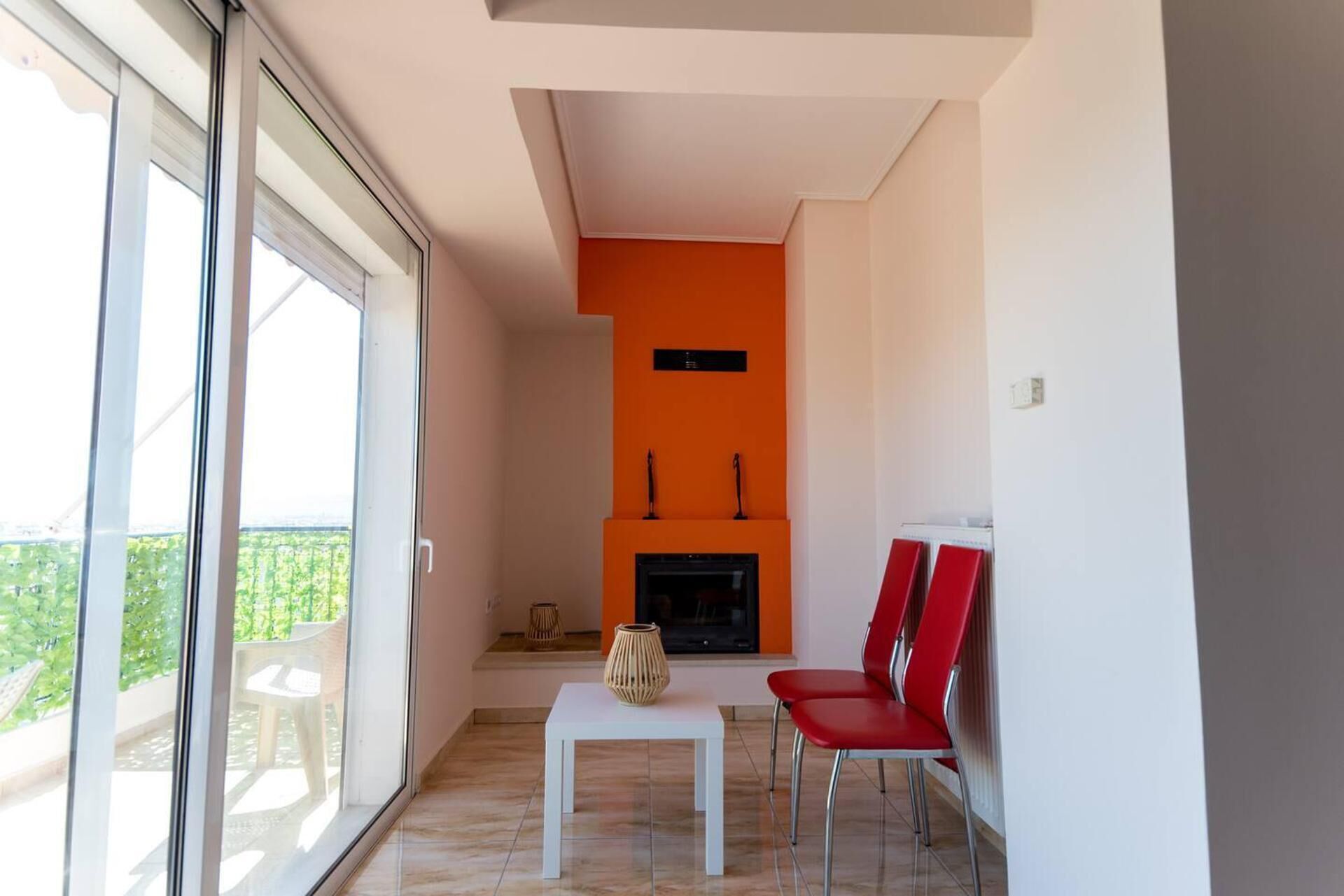 A modern living room with a fireplace, a glass door leading to a balcony, and red chairs.