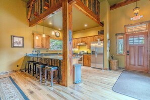 A kitchen with wooden cabinets, a stainless steel refrigerator, and a bar area with stools. - Snow Creek Lodge (West Yellowstone)