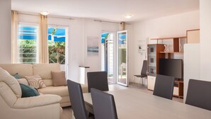 A modern living room with a sofa, a dining table, and chairs. There is a TV and a bookshelf.
