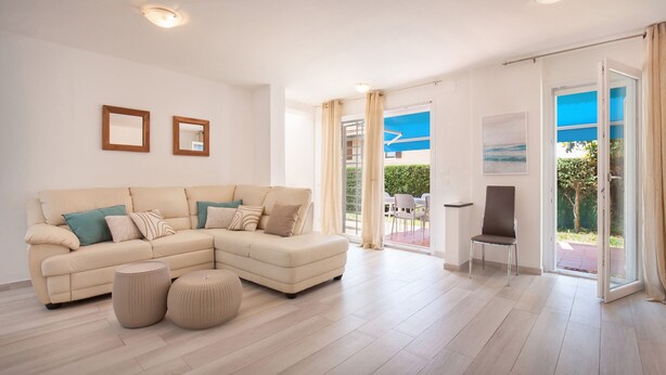 A modern living room with a beige sectional sofa, two small round ottomans, and a glass door leading to an outdoor area.