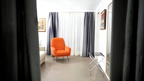 Une pièce avec un canapé blanc, un fauteuil orange, une petite table et un étendoir.