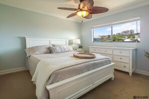 A bedroom with a large bed, a dresser, a window with a view, and a ceiling fan.