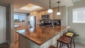 Una cocina moderna con una isla grande, electrodomésticos de acero inoxidable e iluminación colgante.