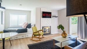 A modern living room with a bed, a fireplace, a TV mounted on the wall, and a window with blinds. - Good Vibes Only * Studio Condo for 2 wifi pool WFH (Gatlinburg)