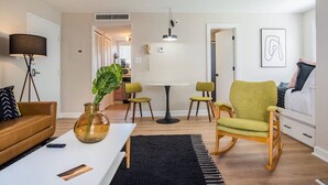 A modern living room with a sofa, a coffee table, a green armchair, and a dining area with a table and chairs. - Good Vibes Only * Studio Condo for 2 wifi pool WFH (Gatlinburg)