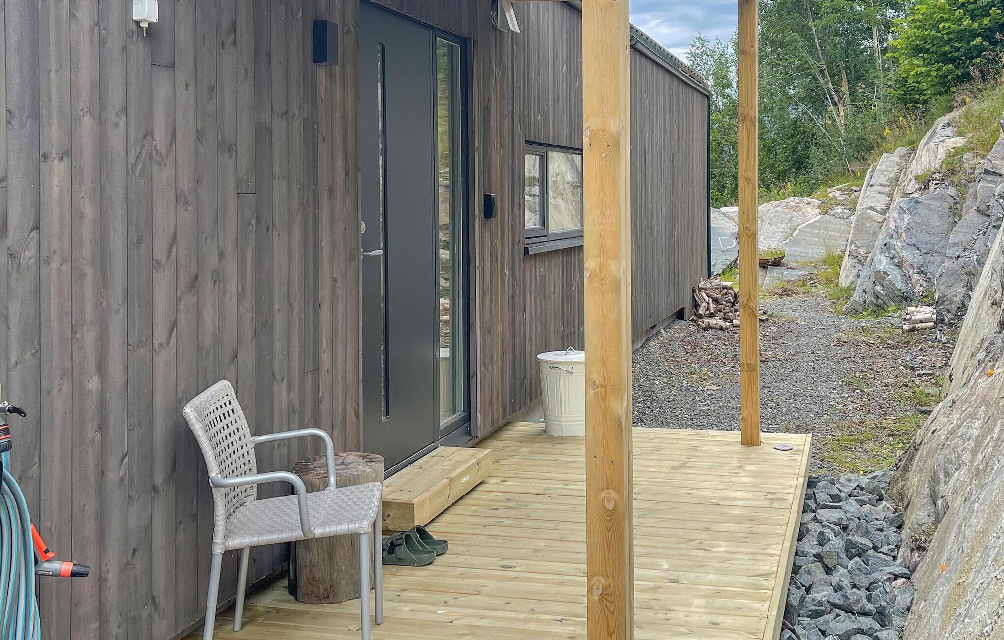 A wooden deck with a chair and a hose, a building with a door and windows, and a rocky outdoor area.